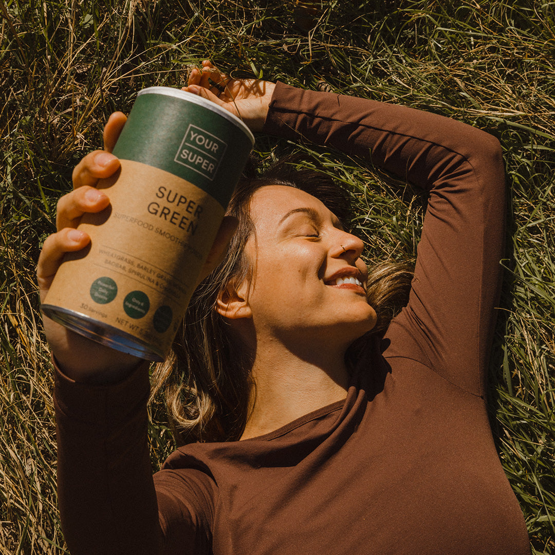 Woman in a brown top lying on a field and holding Your Super Super Green mix